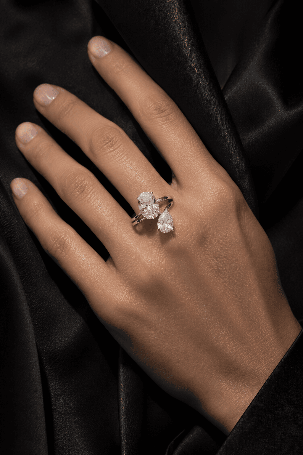 Intricate two-stone diamond engagement ring styled on a hand against black silk